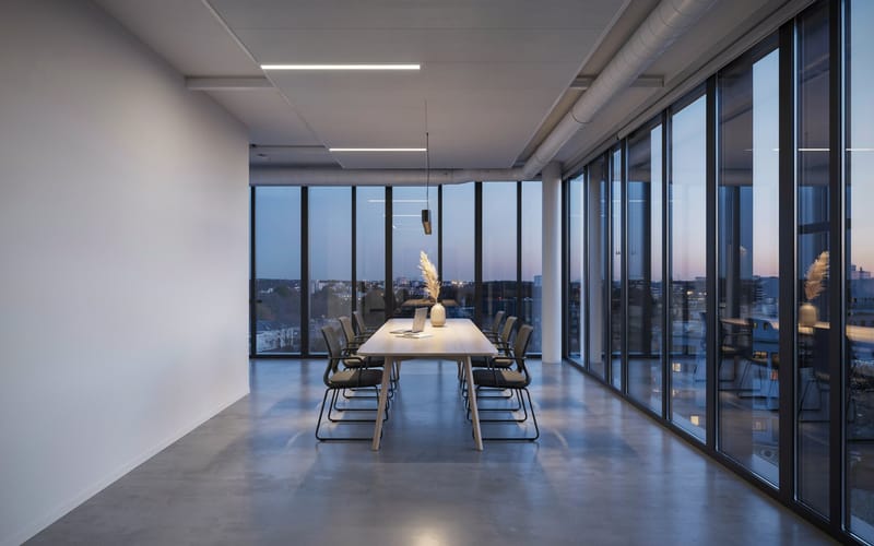 A modern office conference room at dusk with a long table and a city skyline through the windows