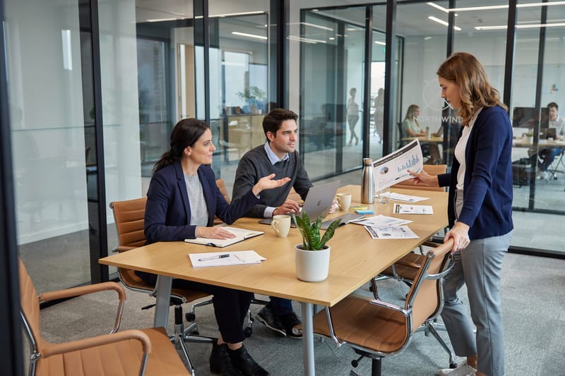 A small team in discussion around a table in a glass-walled office meeting room