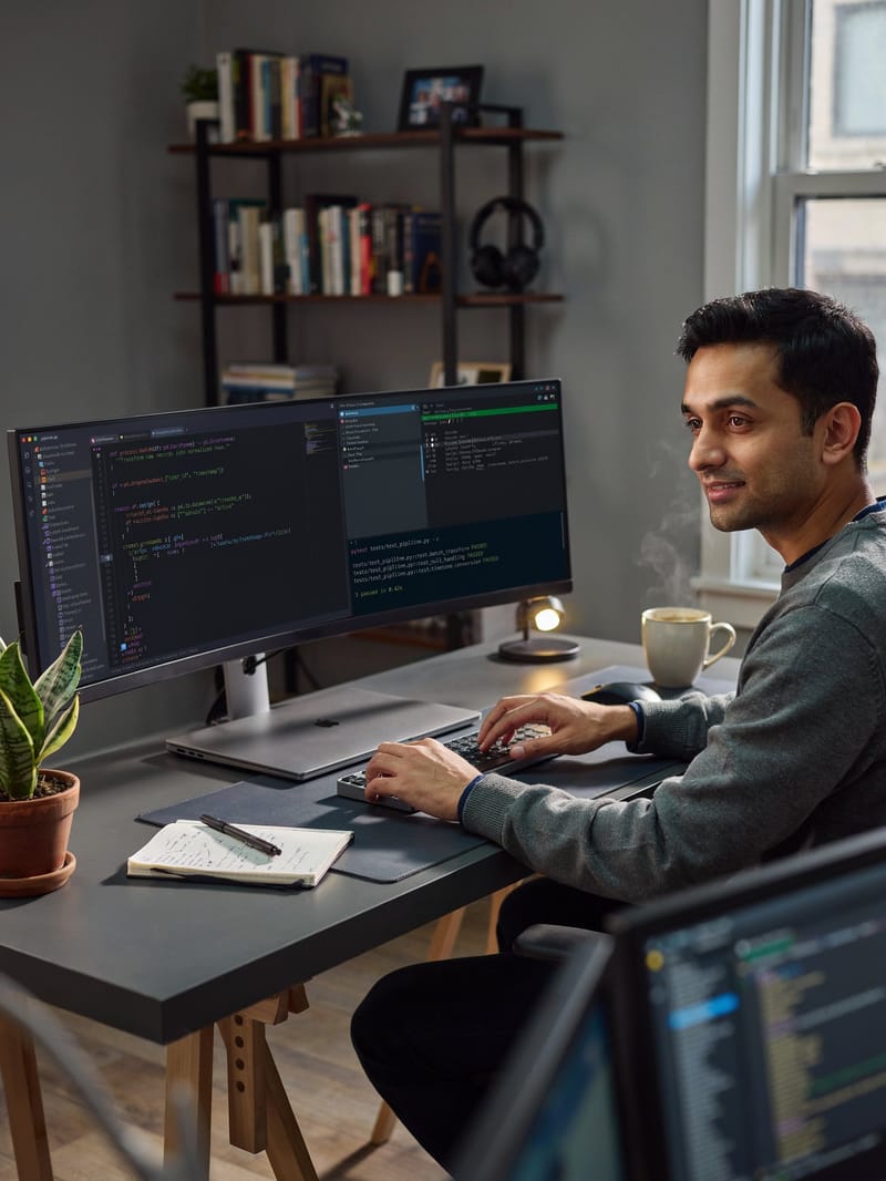 An IT professional working at a desk with dual monitors displaying code