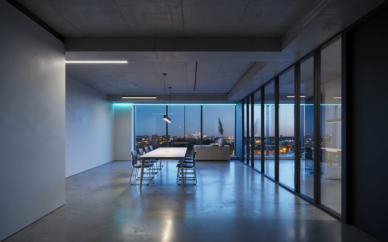 A concrete-floored modern office at night with a meeting table and a city skyline beyond the glass