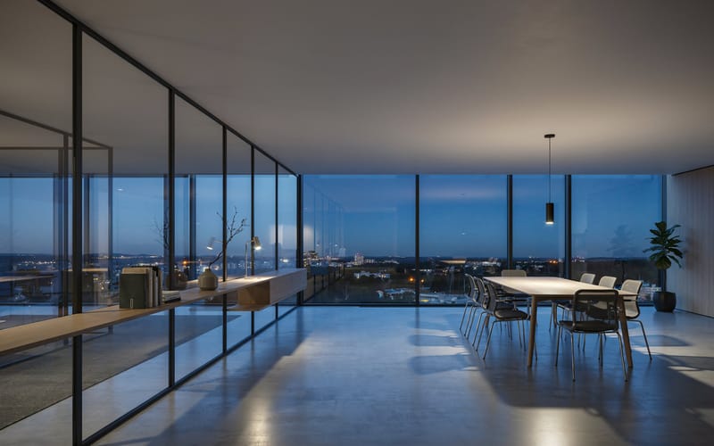 A panoramic office lounge at dusk with a wood credenza and a city skyline through floor-to-ceiling windows